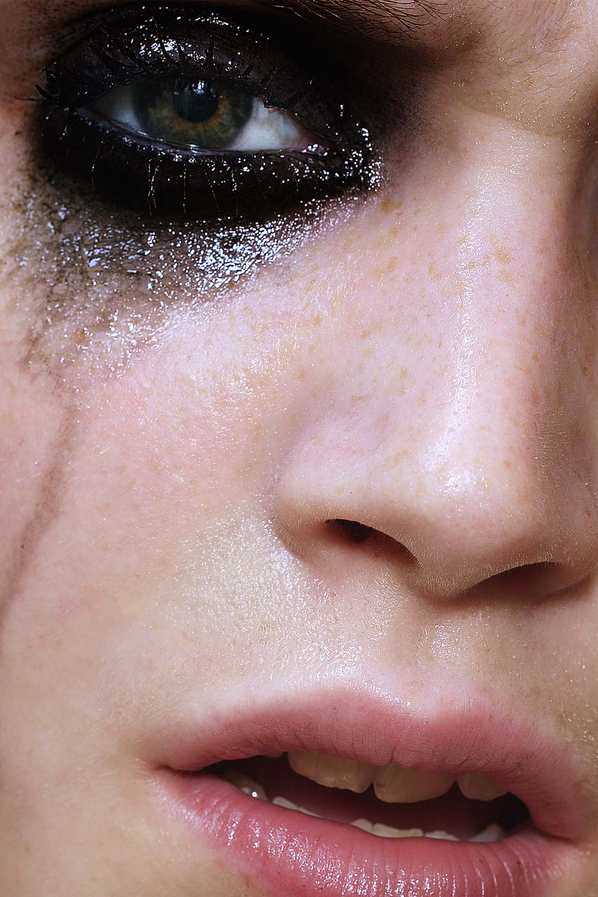 A closeup image of a white womans face. She is wearing dark smudged eyeshadow with silver glitter running down her cheek...