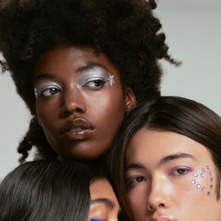  A close-up image of three people of colour wearing glittery makeup.