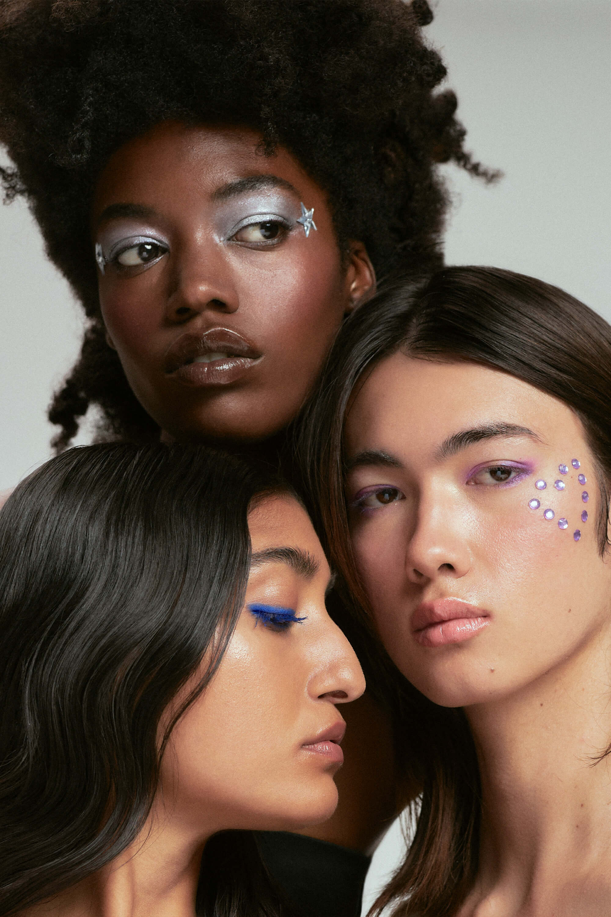 A closeup image of three people of colour wearing glittery makeup.