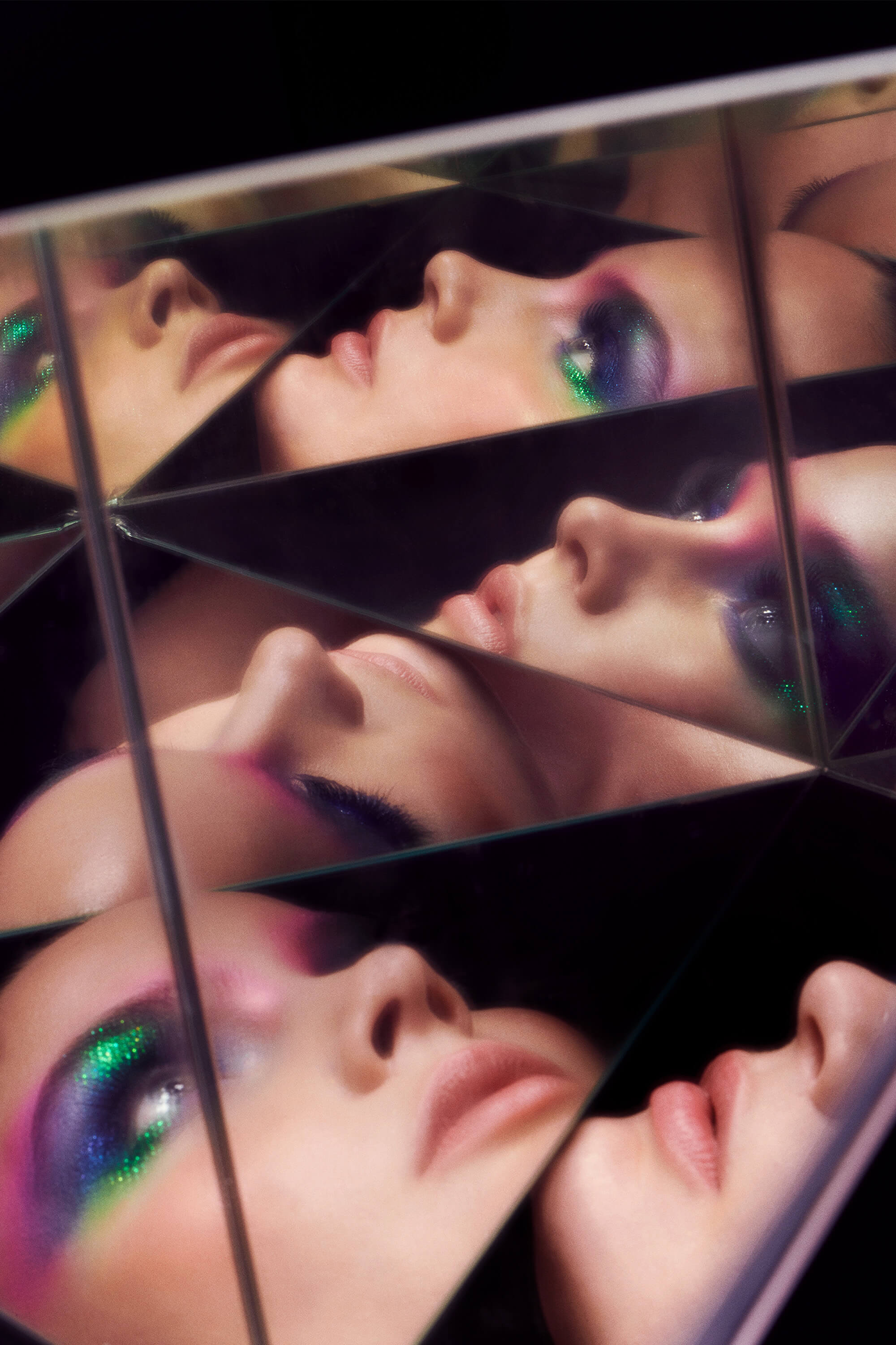 A white woman wearing green blue and pink glittery eyeshadow looks at many reflections of herself.